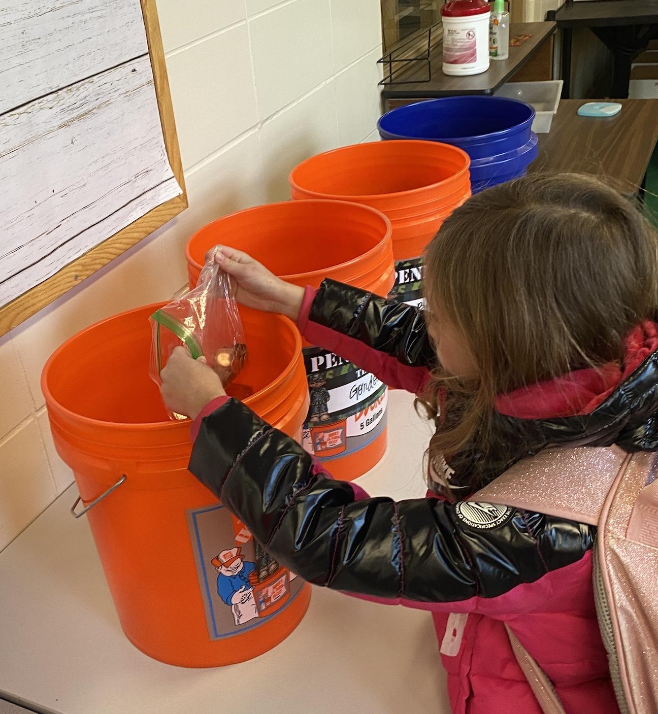 Second-grader Caroline Jenesky adds her coins to her classroom’s bucket