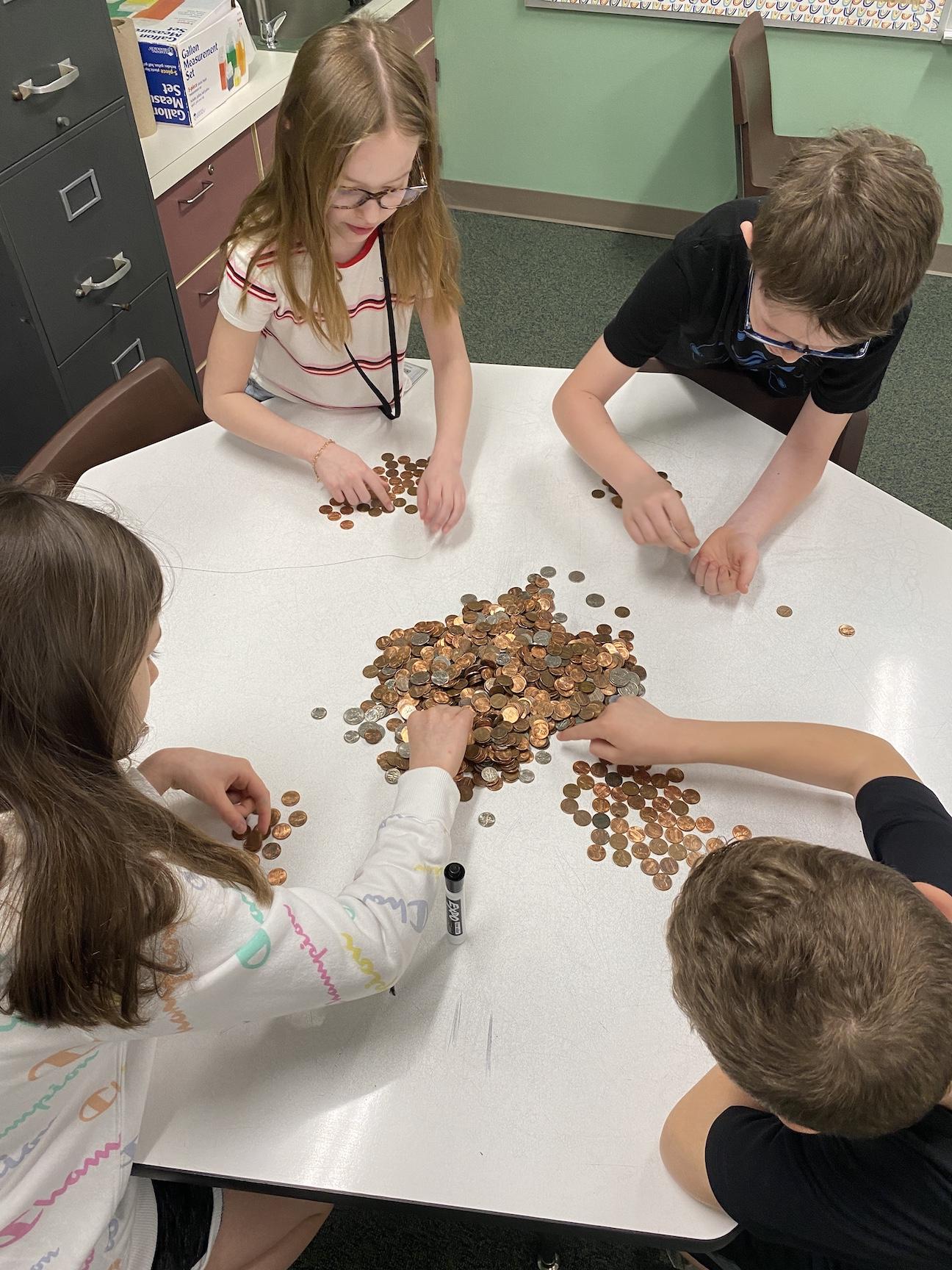 Third-graders Jenna Donis, Jacob Balas, Noah Guthridge, and fourth-grader Taylor Herbert help count coins and determine point values